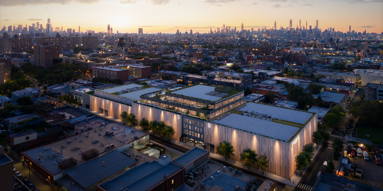 Aerial view of a modern building with a rooftop garden, surrounded by city streets and trees at sunset, with a city skyline in the background under a partly cloudy sky.